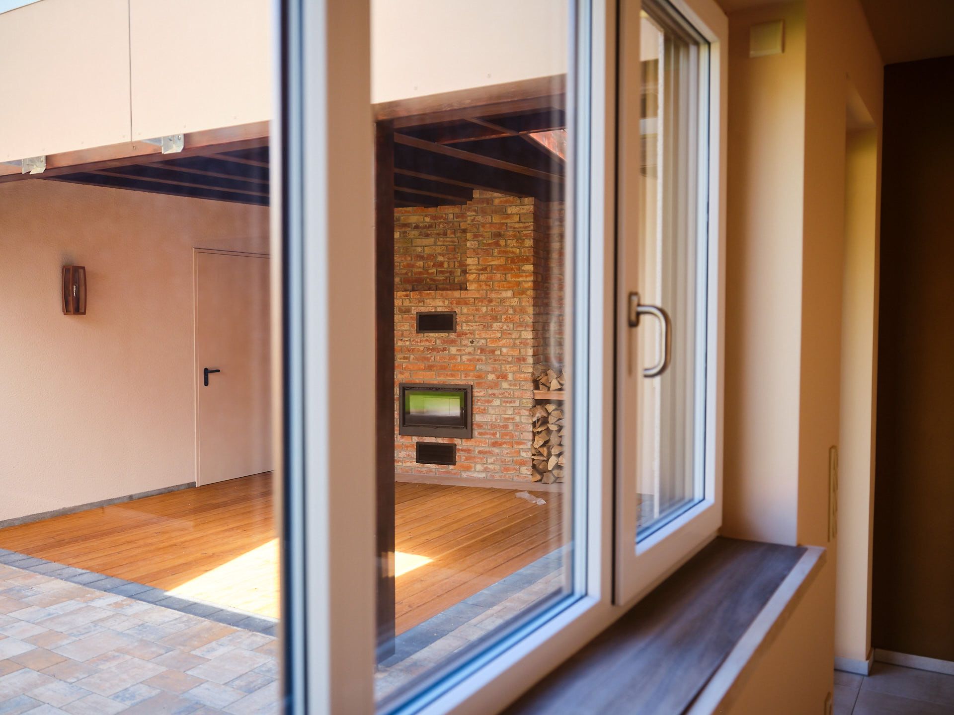 Offener Wohnraum mit gemütlichem gemauertem Kamin, großen Fenstertüren und hochwertigem Echtholzboden.